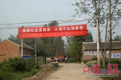 死者的家屬在村口迎接前來吊唁的親友，紅色的橫幅看上去更具諷刺意味。